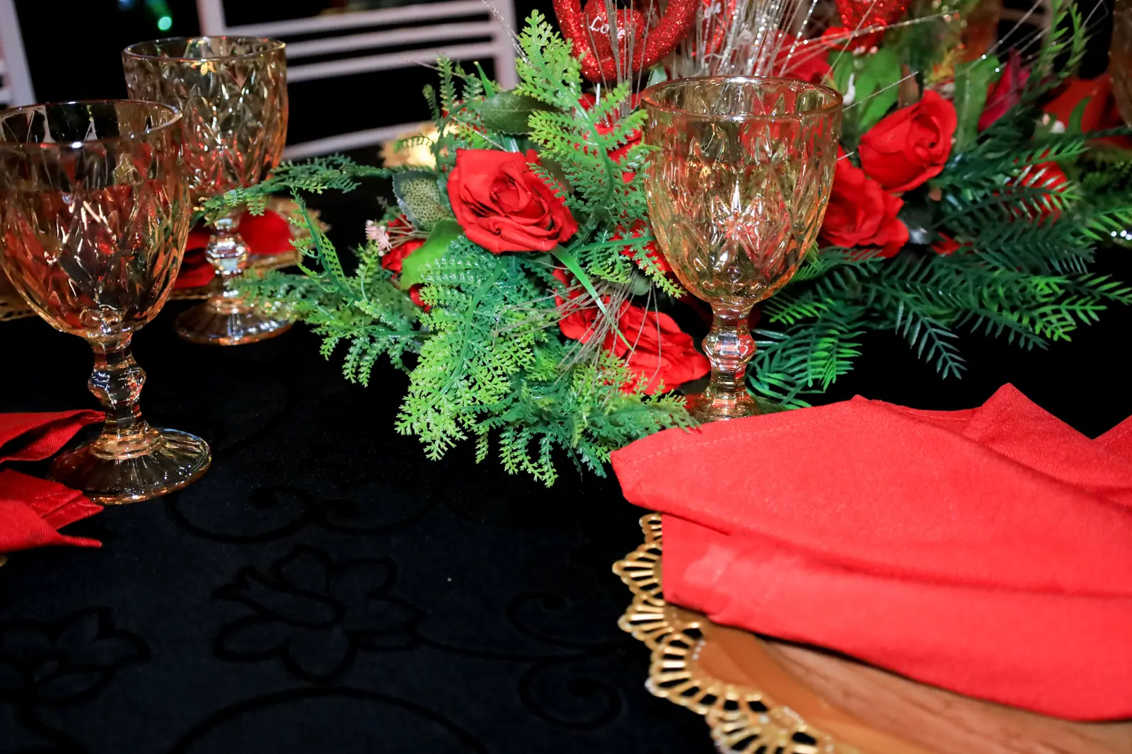 Arranjo floral vermelho e taças na mesa dos convidados